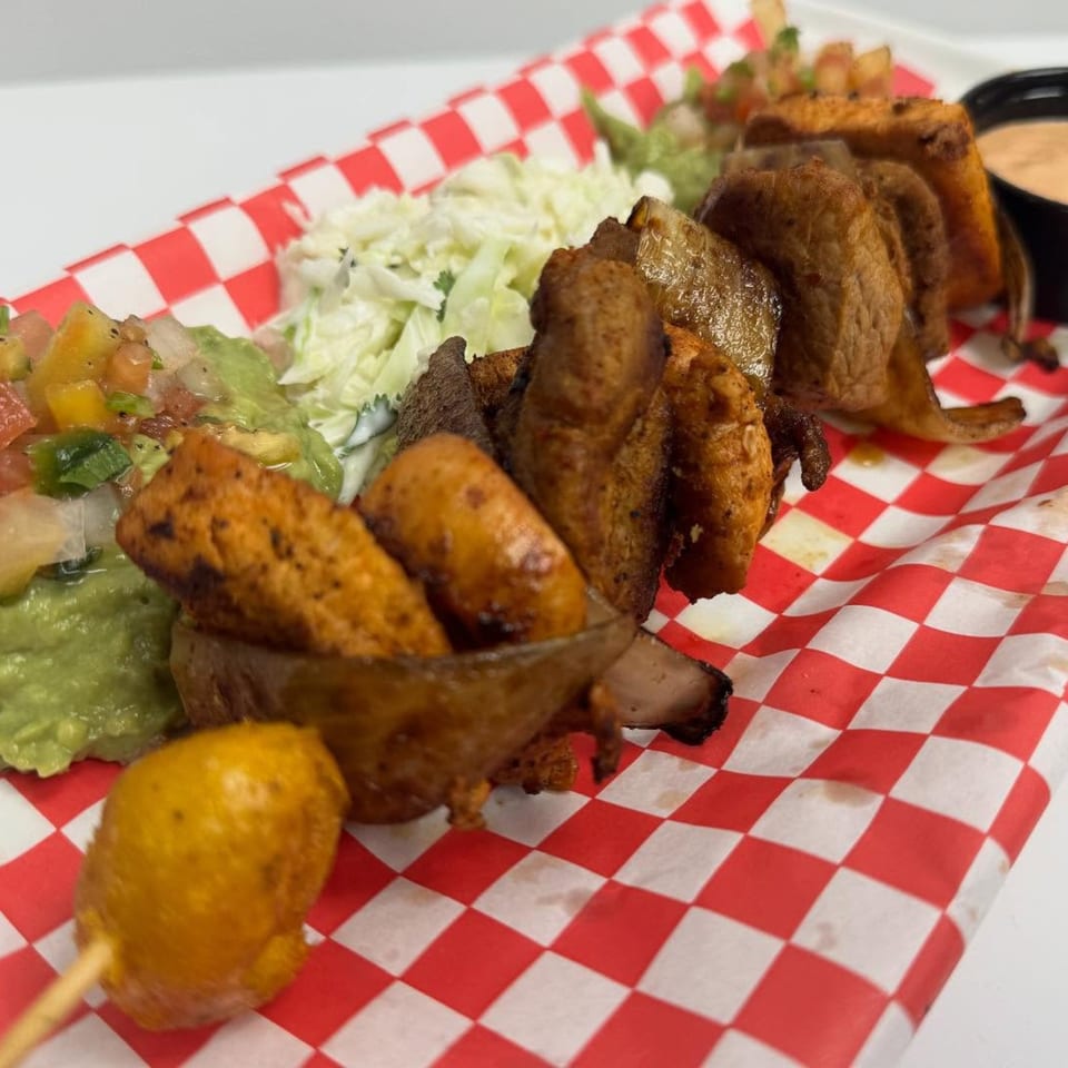 A platter of Mexican food with fried plantains, guacamole, salsa, and coleslaw on red and white checkered paper.