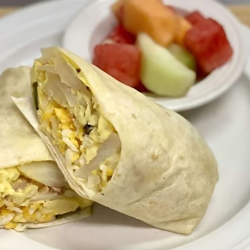 Two breakfast burritos filled with eggs and potatoes, served with a side of fresh fruit.