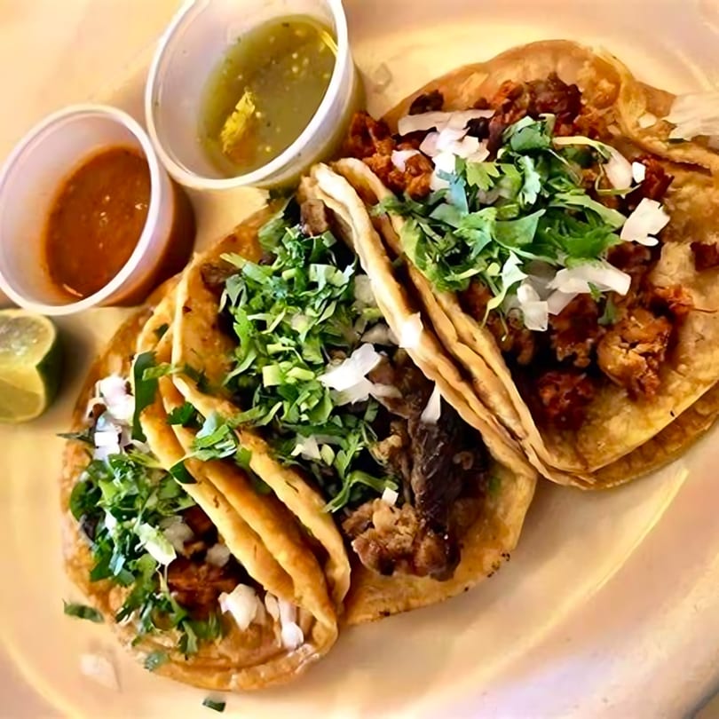 Three Dos Reales Mexican street tacos with meat, cilantro, and onions, served with two salsas and lime.