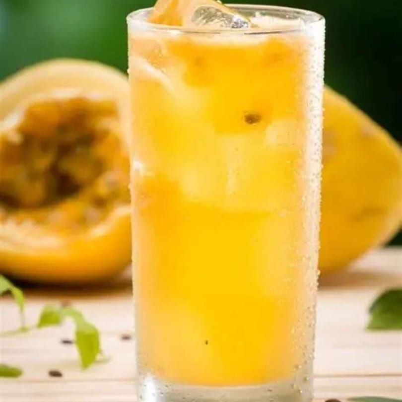 A tall glass of iced passion fruit juice with a halved passion fruit in the background.