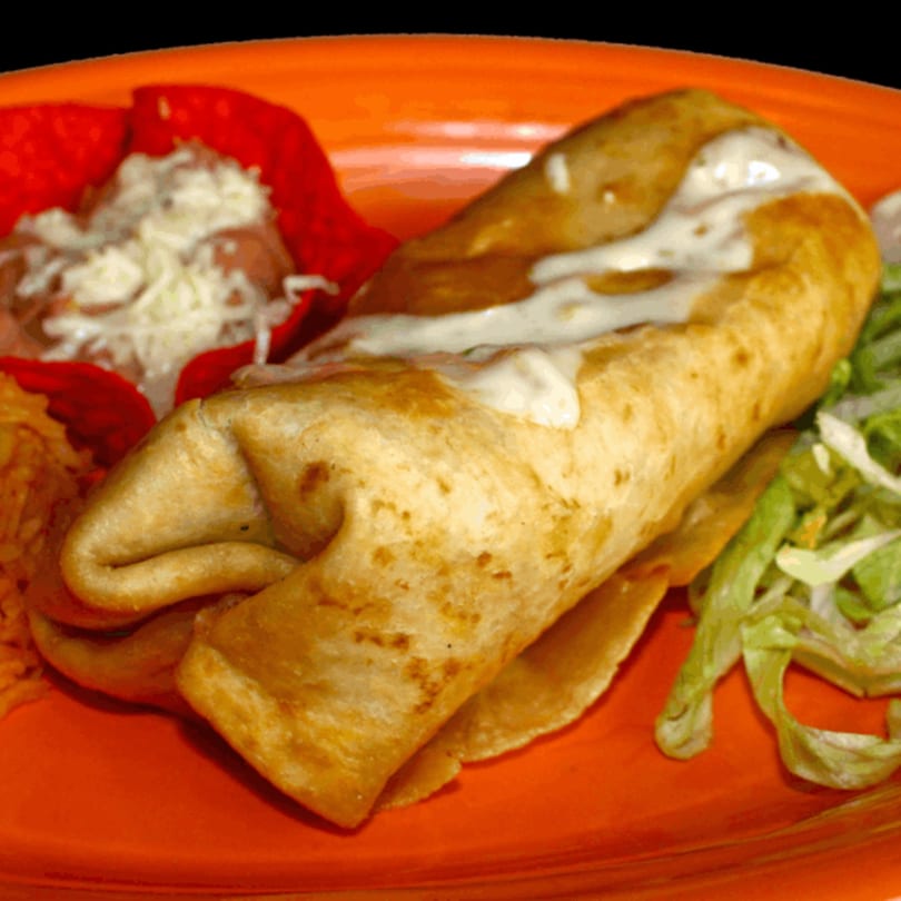 A golden-brown chimichanga drizzled with white sauce, served with rice, beans, and lettuce on an orange plate.