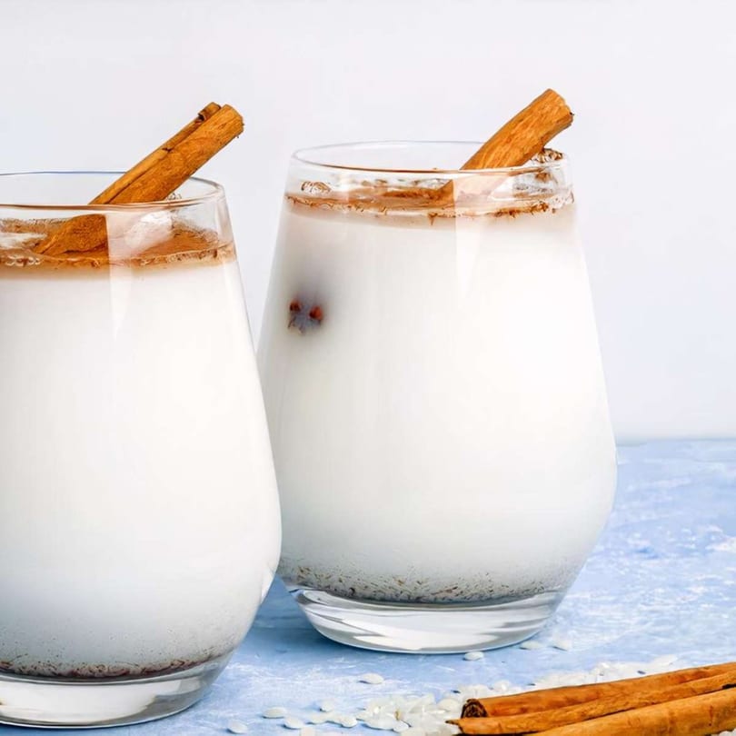 Two glasses of horchata, a traditional Mexican drink, garnished with cinnamon sticks and powder.