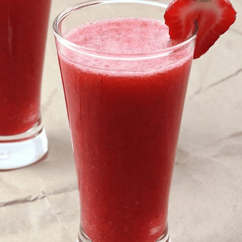 A vibrant red strawberry smoothie in a tall glass, garnished with a fresh strawberry slice.