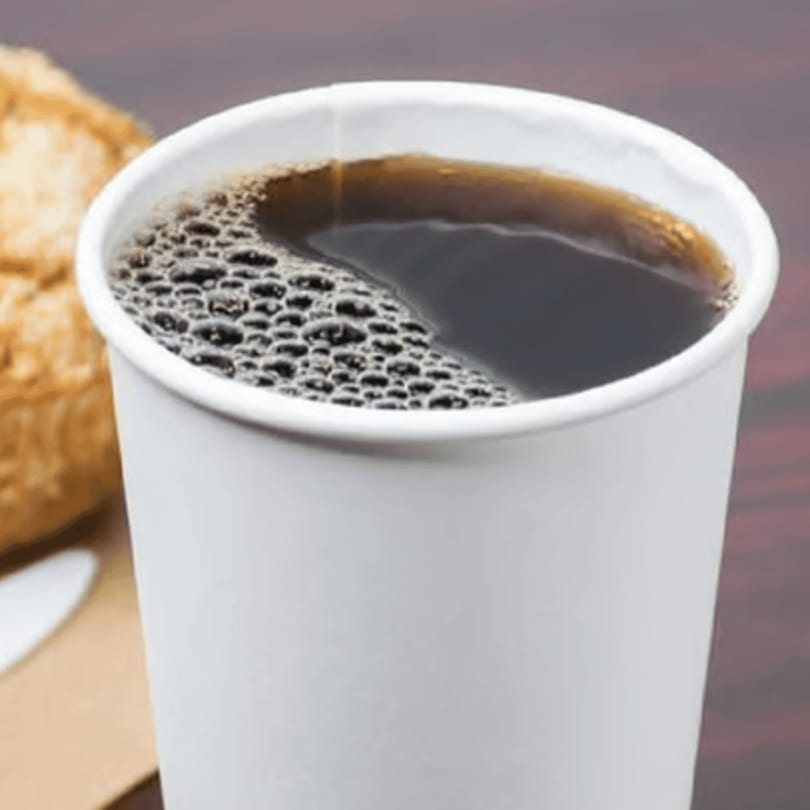 Close-up of a white paper cup filled with dark coffee, showing small bubbles on the surface.