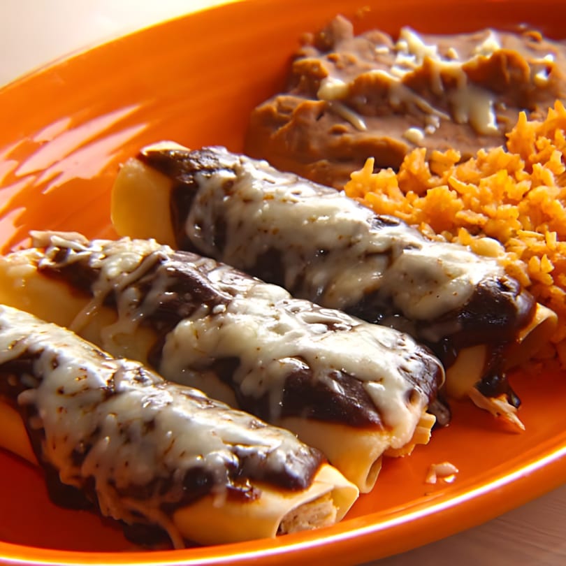 Three enchiladas with mole sauce and melted cheese, served with refried beans and Mexican rice.