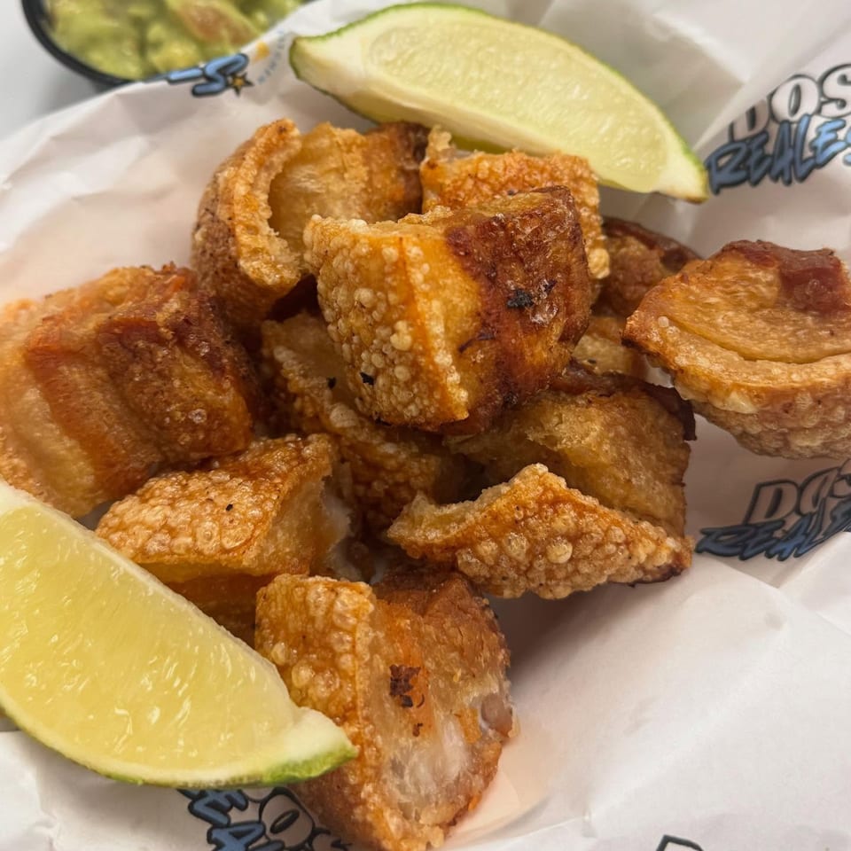 Crispy chicharrones with lime wedges and a side of guacamole from Dos Reales Latin Kitchen.